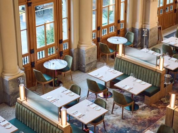 Elegant Brasserie Süd interior featuring plush green velvet seating, modern marble-top tables, large wooden windows, and a unique cosmic-patterned floor, creating a chic and inviting dining ambiance.