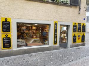 Traditional shop exterior, potentially Bierhalle Wolf's specialty food or deli counter, adorned with yellow cutting board-shaped menu signs, a wide display window revealing its interior, and an inviting entrance on a cobblestone street.