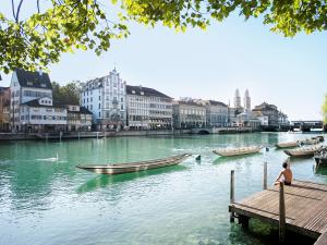 Serene Limmatquai in Zürich, showcasing the turquoise Limmat River with traditional boats, historic waterfront buildings, and a person relaxing on a sunny wooden dock.