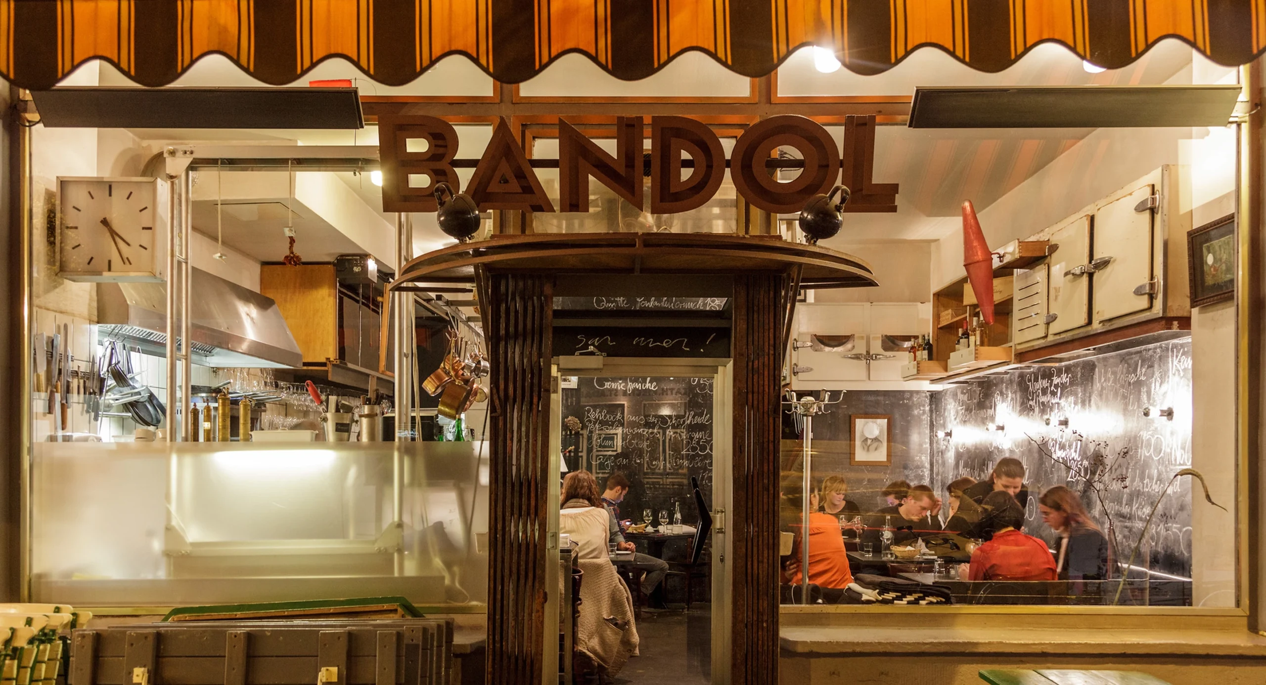 Bandol restaurant exterior at night, featuring its prominent sign and visible kitchen, with patrons dining inside in Bandol sur Mer.