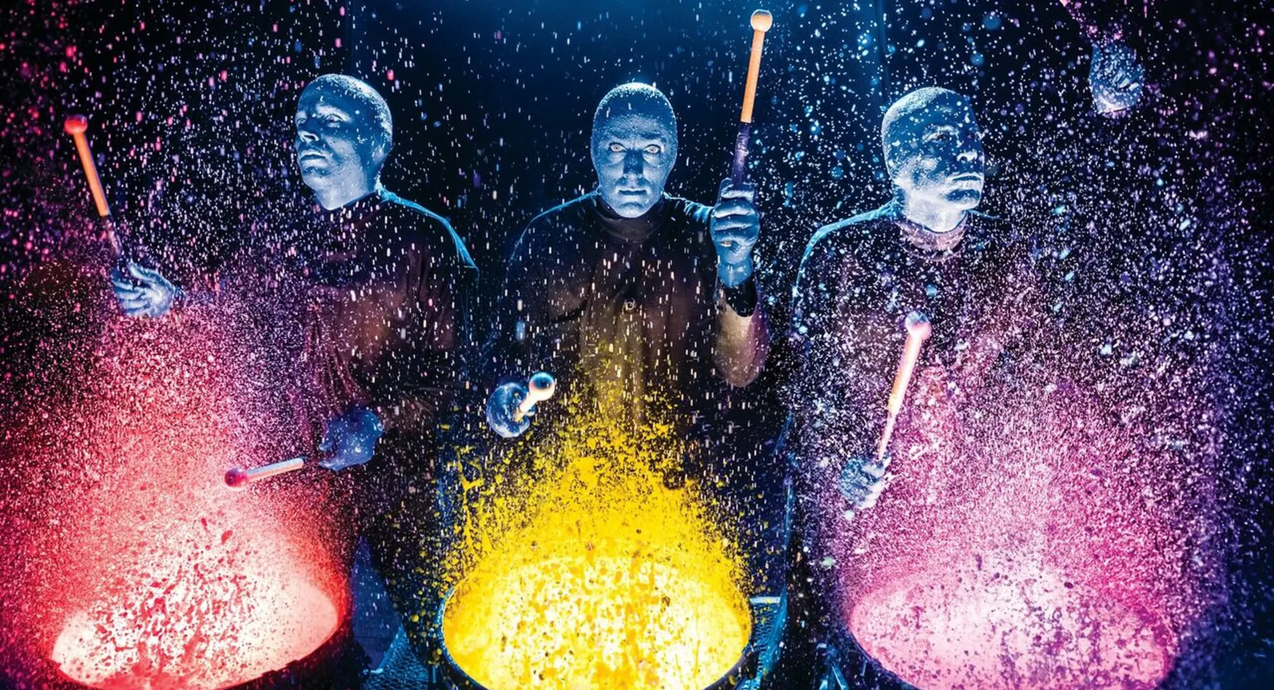 Blue Man Group performers creating vibrant multi-colored paint splashes from percussion instruments during their captivating live show experience.