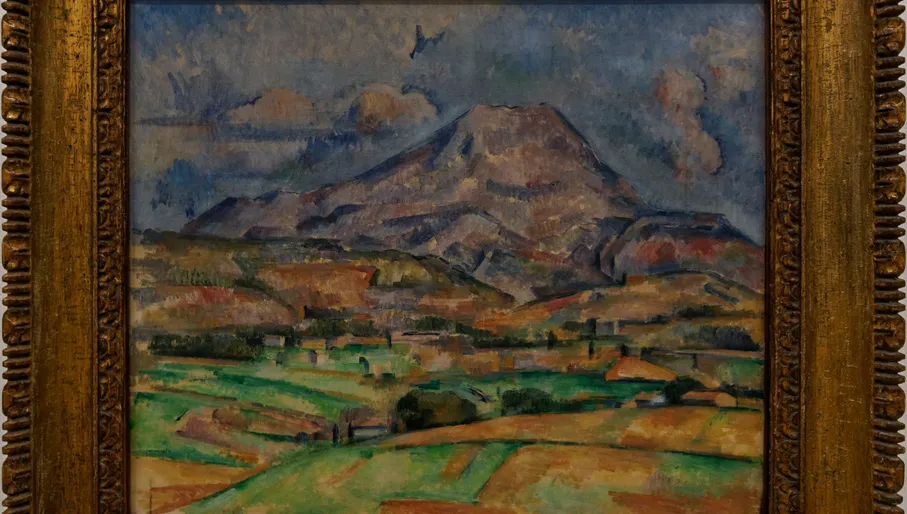 Paul Cézanne's iconic Mont Sainte-Victoire landscape painting, featuring the majestic mountain above green fields and houses, displayed in a gold ornate frame, a must-see masterpiece in Amsterdam.