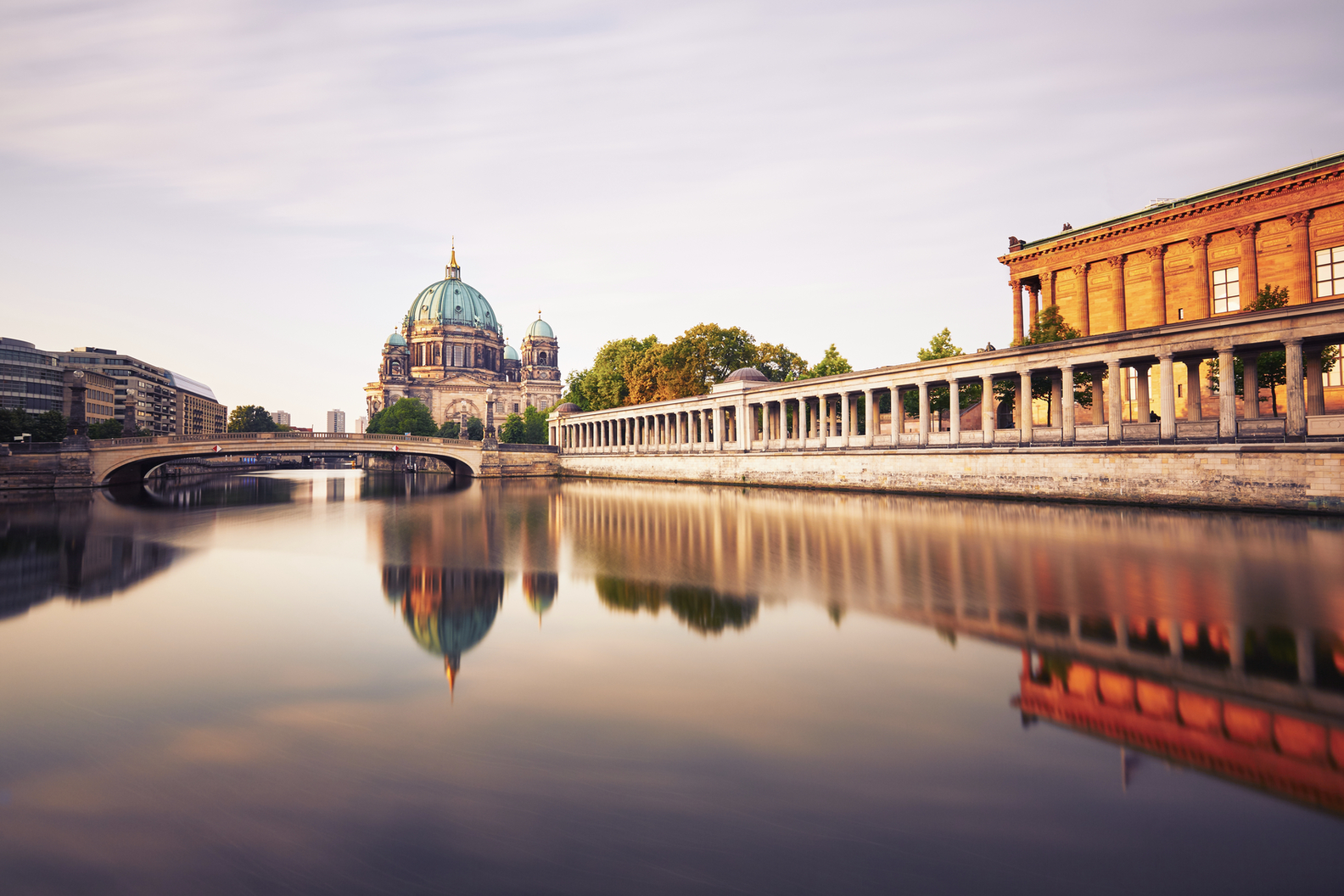 Iconic Berlin Cathedral and Museum Island reflecting on the tranquil Spree River under warm morning sunshine.