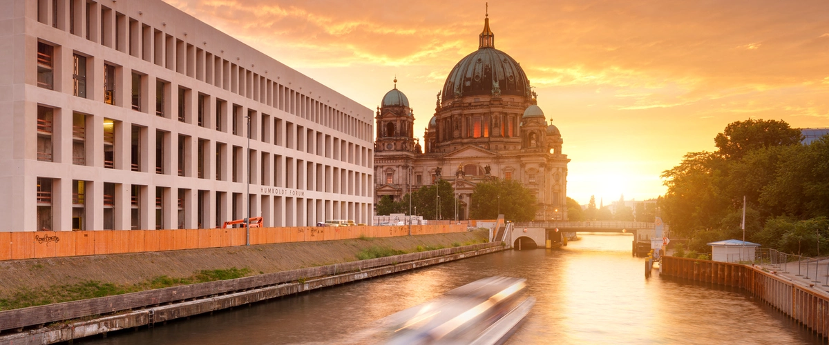 Berlin evening boat tour view of the historic Berlin Cathedral and Humboldt Forum on the Spree River, illuminated by a vibrant sunset, setting the scene for the Festival of Lights.