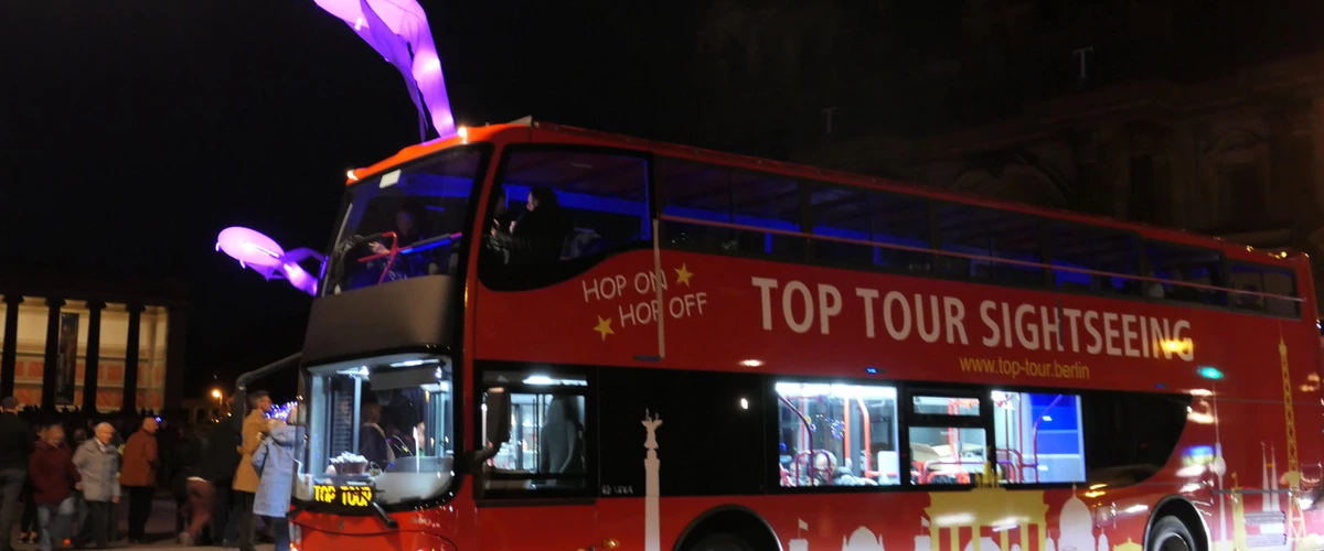 Red TOP TOUR SIGHTSEEING hop-on hop-off double-decker bus illuminated with purple lights for a Berlin Festival of Lights night tour.