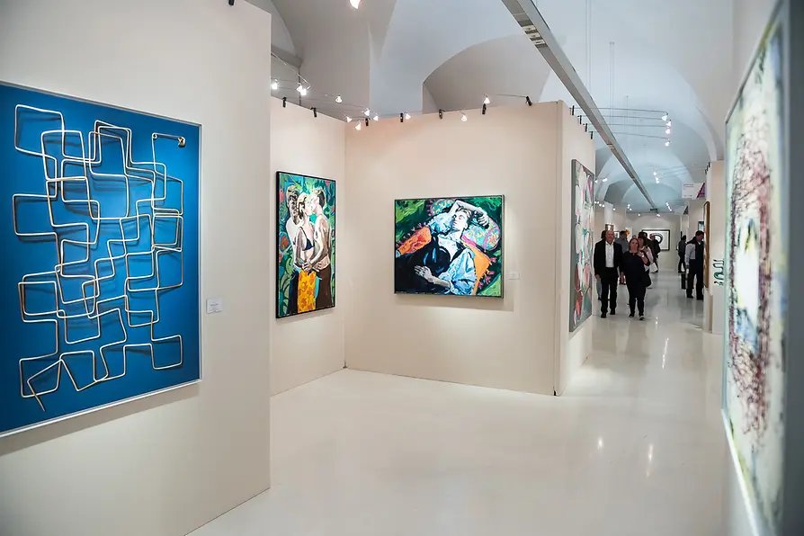 Bustling Fair For Art Vienna exhibition showcasing diverse contemporary paintings and a distinctive blue geometric wall sculpture within an arched gallery space.