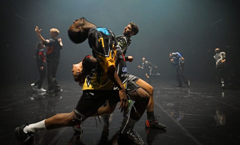 Dynamic athletic dancers performing a contemporary or hip-hop routine on a dark, reflective stage, with one male dancer in a deep backbend, featured in The Week August 4-24, 2025.