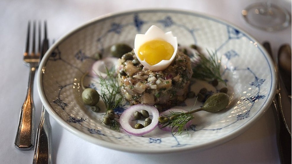 Danish herring tartare with soft egg yolk, capers, red onion, and dill, served on a patterned plate at Schønnemann's restaurant.