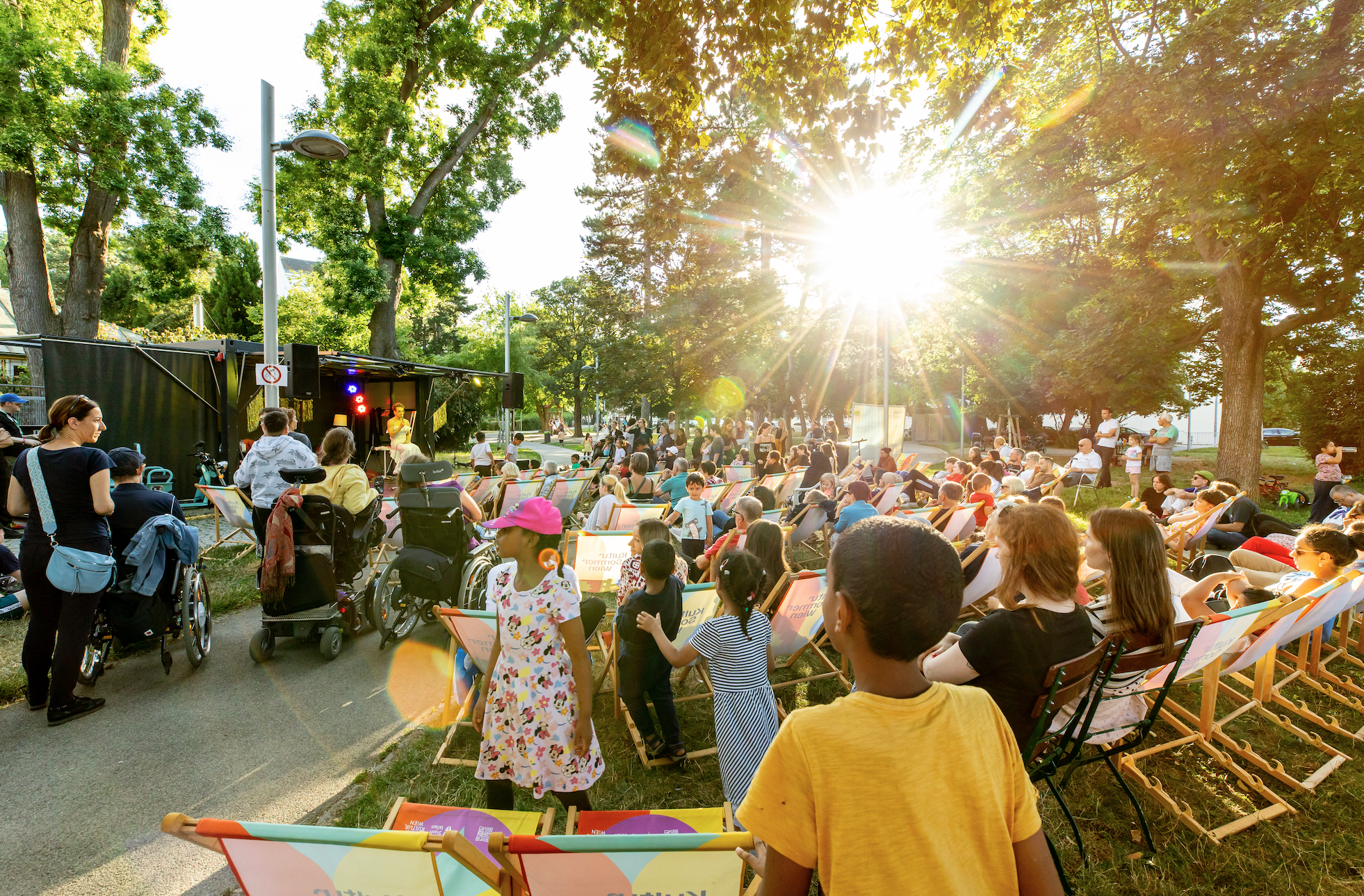 Sunny open-air performance in a Vienna park, with a diverse audience enjoying the event from colorful deck chairs, typical of Vienna's best summer events in June.