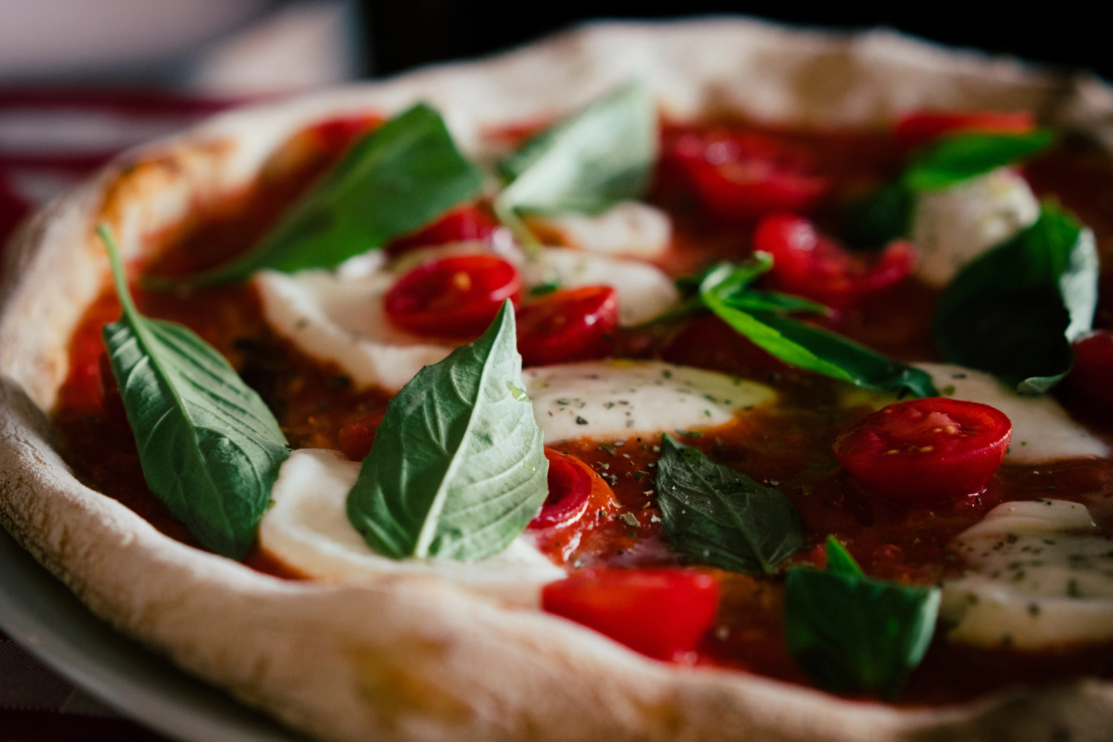 Artisanal pizza topped with fresh basil, sliced cherry tomatoes, and melted mozzarella.