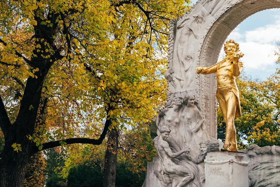Golden Johann Strauss Monument in Vienna's Stadtpark surrounded by autumn leaves, a significant landmark on the audio walk.