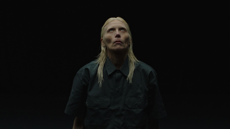 Dramatic video art still featuring a blonde figure with long hair in a dark shirt looking upwards, from the Julia Stoschek Foundation Berlin collection.