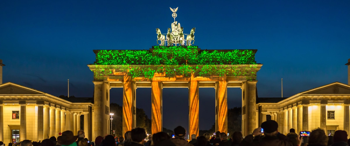 Brandenburg Gate illuminated with vibrant green foliage and orange light projections during the Berlin Festival of Lights, captured on a lightseeing walking tour.