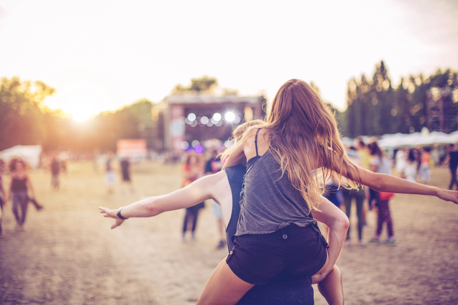 Enthusiastic festivalgoer on shoulders enjoying Lollapalooza Berlin summer music festival at sunset.