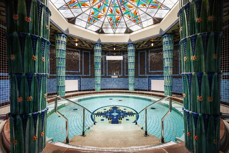 Vienna's Amalienbad Art Nouveau public bath, featuring an ornate mosaic pool, decorative tiled pillars, and a vibrant stained glass dome.
