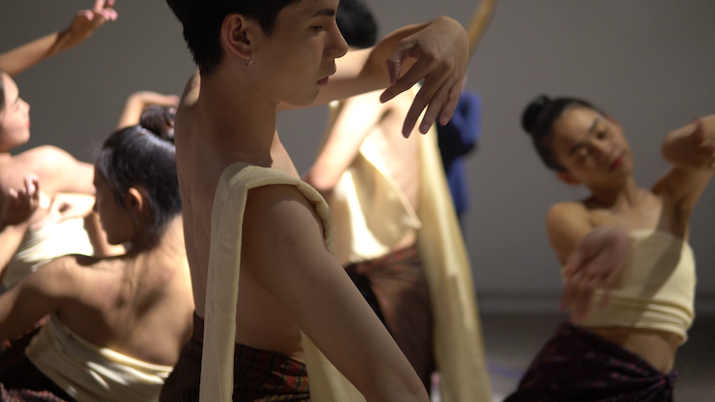 Male dancer with expressive hand gestures, performing alongside female ensemble in traditional-inspired costumes, at Tanz im August 2025.