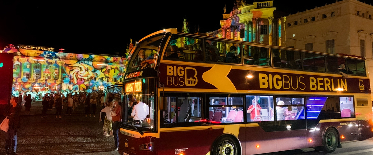 Big Bus Berlin double-decker tour bus at night with passengers, viewing vibrantly illuminated buildings during the Festival of Lights in Berlin.